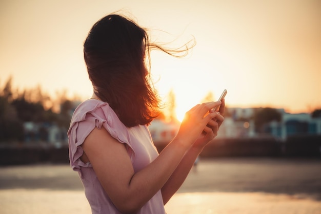 Vista laterale di una donna adulta che usa uno smartphone mentre si trova di fronte al cielo durante il tramonto