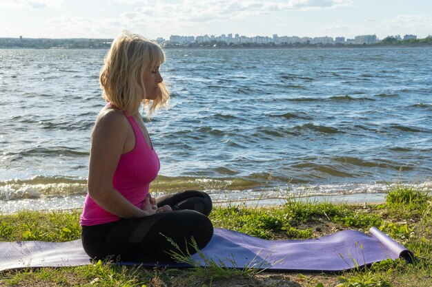 Vista laterale di una donna anziana seduta nell'Ardha Padmasana posa una posa yoga mezzoloto su una stuoia