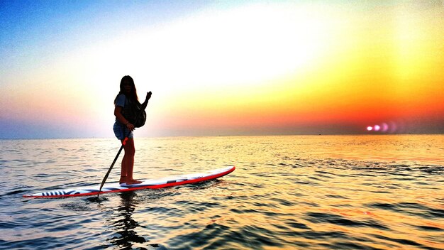 Vista laterale di una donna che fa paddleboard sul mare contro il cielo durante il tramonto