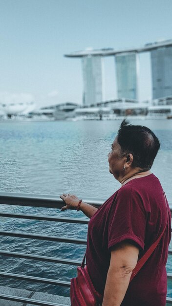 Vista laterale di una donna che guarda il mare mentre si trova davanti a una ringhiera contro il cielo