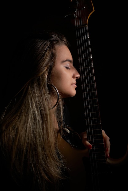 Vista laterale di una donna che tiene la chitarra contro uno sfondo nero