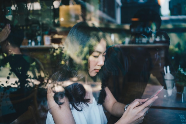 Vista laterale di una donna che usa il telefono cellulare mentre è seduta a tavolo vista attraverso una finestra di vetro