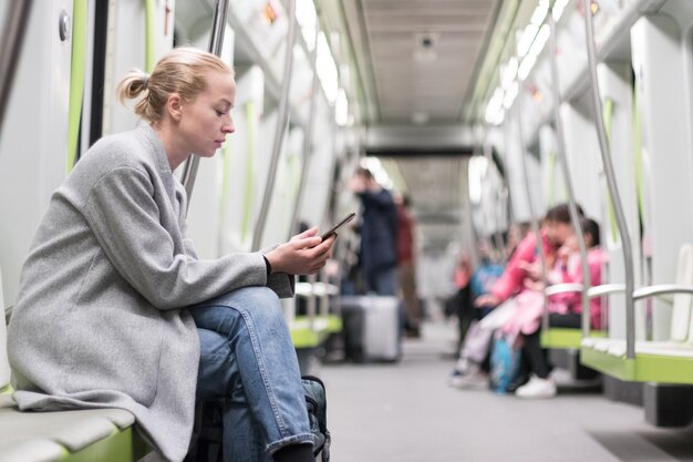 Vista laterale di una donna che usa uno smartphone seduta nel treno della metropolitana.