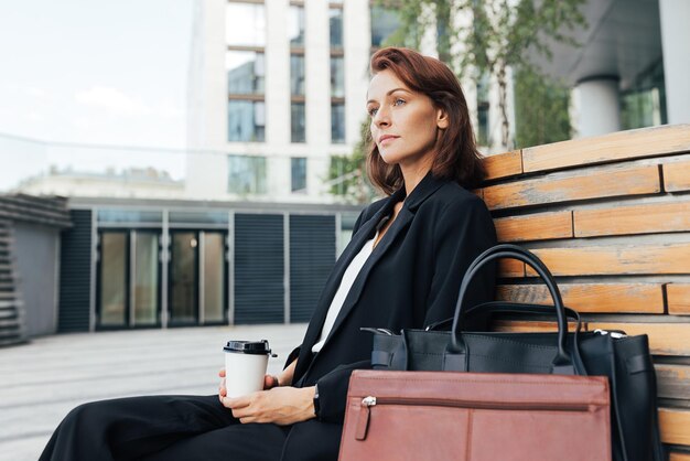 Vista laterale di una donna d'affari di mezza età seduta all'aperto con un caffè in mano