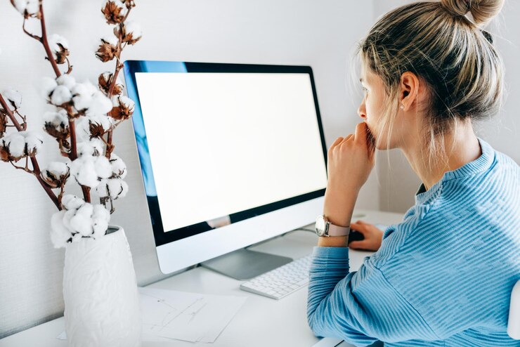 Vista laterale di una donna d'affari freelance che utilizza il computer desktop in un ufficio creativo Foto di una giovane donna bionda seduta in casa a lavorare al computer con uno schermo vuoto per il messaggio di testo o il contenuto