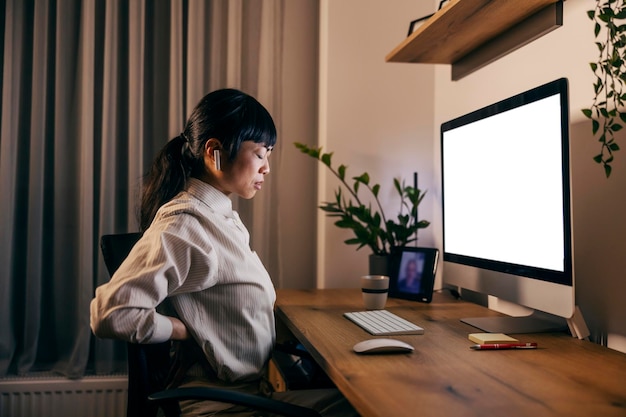 Vista laterale di una donna d'affari giapponese che lavora fino a tardi in ufficio a casa e ha mal di schiena