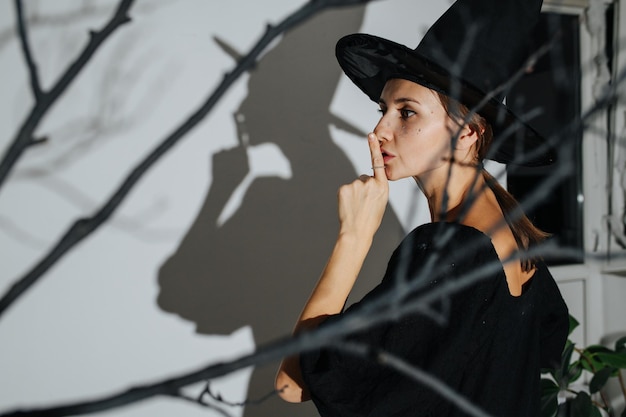 Vista laterale di una donna in costume da strega che fa un gesto zitto che getta ombra