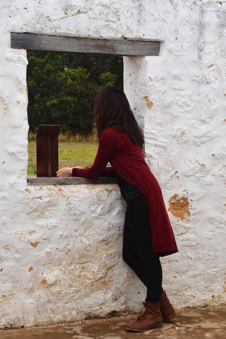 Foto vista laterale di una donna in piedi contro il muro che guarda fuori da una finestra