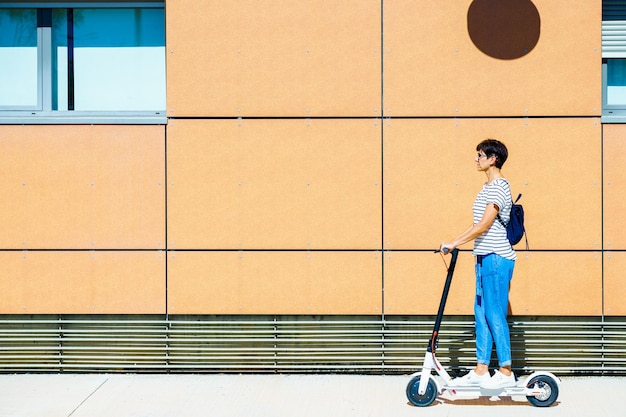 Vista laterale di una donna in piedi su uno scooter elettrico contro l'edificio