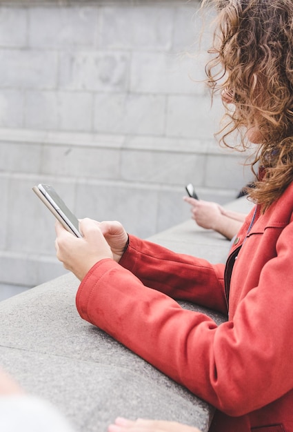 Vista laterale di una donna matura che usa uno smartphone mentre è in piedi vicino al muro di sostegno