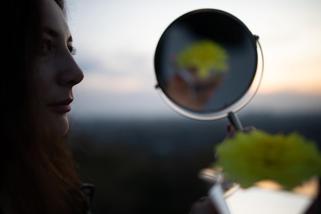 Vista laterale di una donna pensierosa in piedi davanti allo specchio contro il cielo durante il tramonto