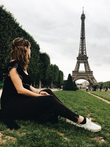 Vista laterale di una donna seduta su un campo erboso contro la Torre Eiffel in città