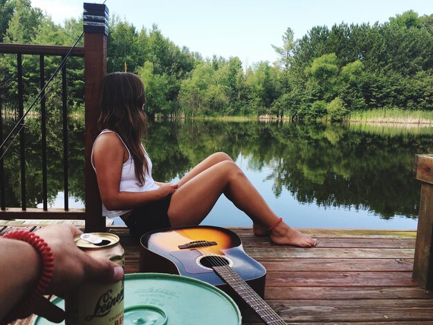 Vista laterale di una donna seduta sul molo al lago contro gli alberi