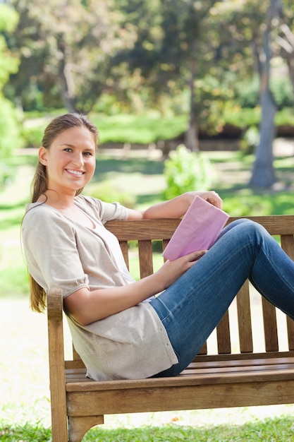 Vista laterale di una donna sorridente con un libro su una panchina