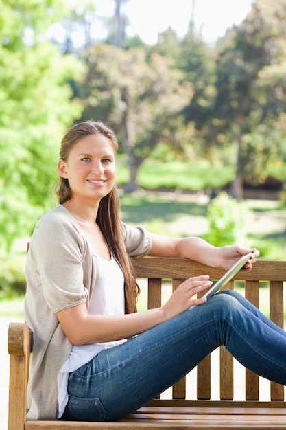 Vista laterale di una donna sorridente con un tablet PC su una panchina