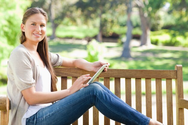 Vista laterale di una donna sorridente utilizzando un tablet PC su una panchina