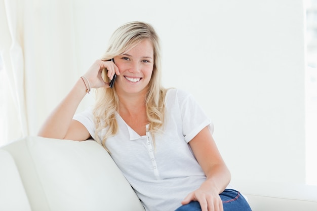 Vista laterale di una donna sul suo divano sorridente mentre parla al telefono