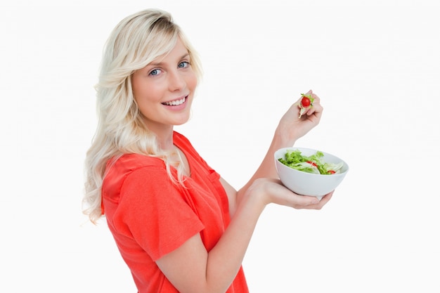 Vista laterale di una giovane donna che mostra un grande sorriso mentre si mangia insalata
