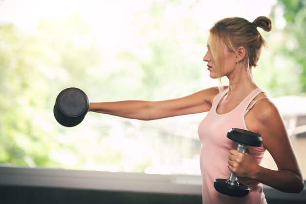 Vista laterale di una giovane donna che si esercita con i manubri in palestra