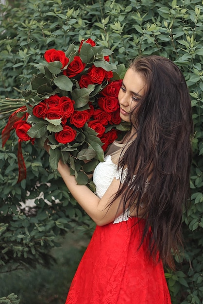Vista laterale di una giovane donna che tiene un bouquet di rose mentre si trova accanto alle piante