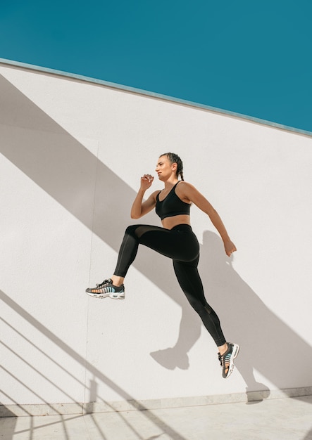 Vista laterale di una giovane donna fitness in abbigliamento sportivo Sport che saltano come correre