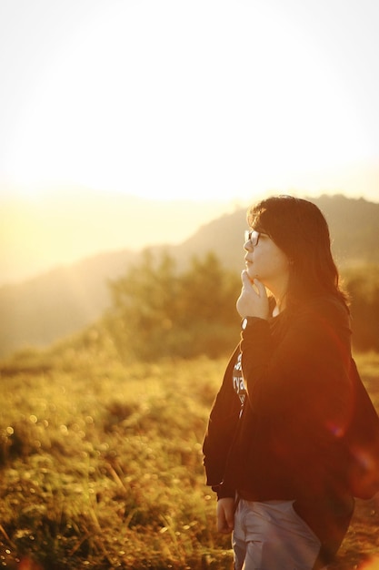 Vista laterale di una giovane donna in piedi sul campo durante il tramonto