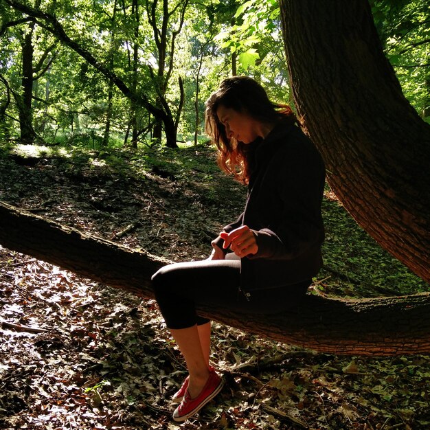 Vista laterale di una giovane donna seduta su un tronco nella foresta