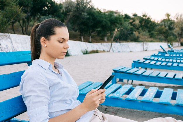 Vista laterale di una giovane donna sulla spiaggia leggendo un libro seduto sulla panchina