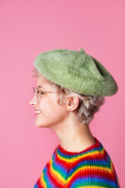 Vista laterale di una ragazza carina che indossa un maglione arcobaleno e un berretto verde su uno sfondo rosa