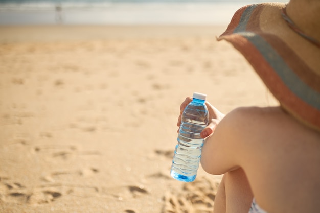 Vista laterale di una ragazza sulla spiaggia con in mano una bottiglia di acqua minerale.