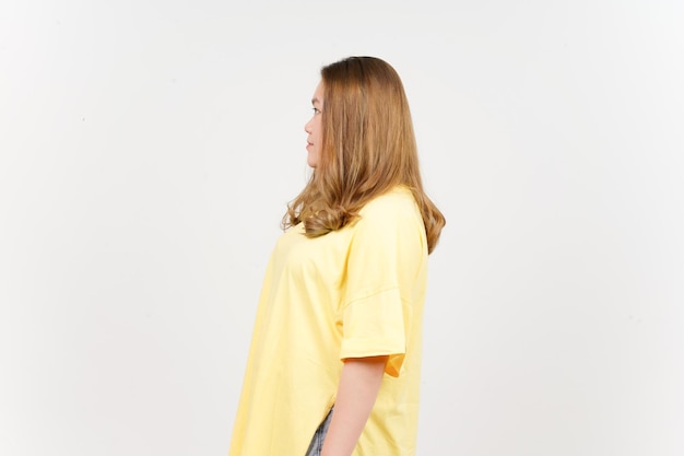 Vista laterale in piedi di bella donna asiatica che indossa una maglietta gialla isolata su sfondo bianco