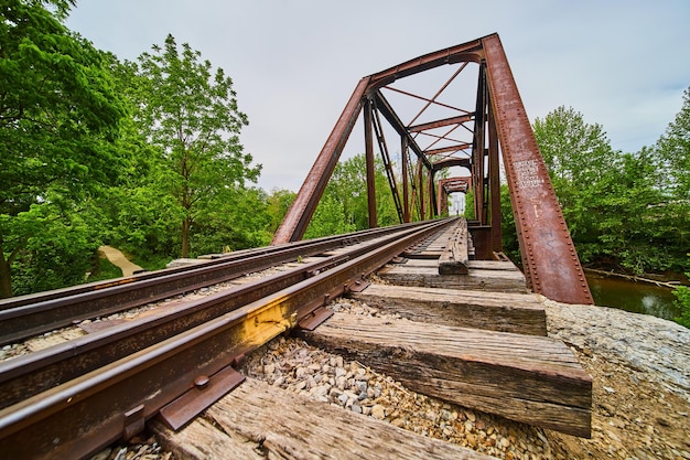 Vista laterale inclinata dei binari del treno con travi di legno sotto i binari che portano al ponte ferroviario