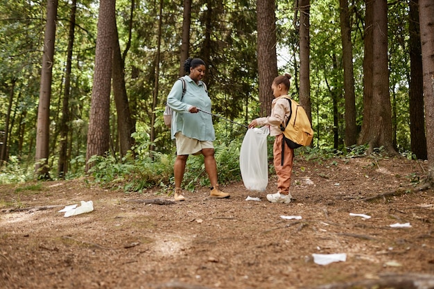 Vista laterale madre e figlia che raccolgono bottiglie di plastica sul sentiero natura