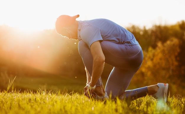 Vista laterale orizzontale del giovane velocista maschio in forma che lega i lacci delle scarpe prima di iniziare a correre nel parco Atleta Handosme che corre all'aperto preparandosi per la maratona in montagna Concetto di persone sportive