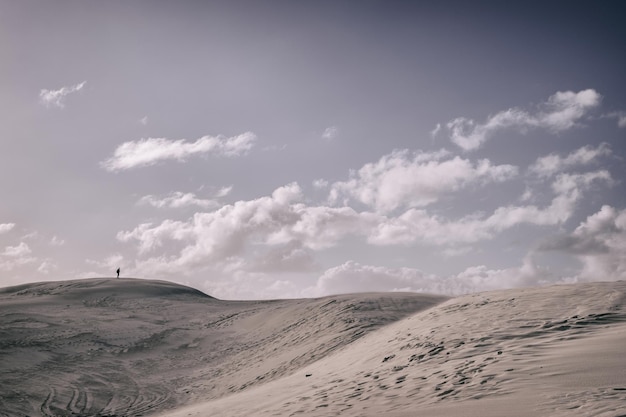 Vista lontana di una persona in piedi su dune di sabbia contro il cielo
