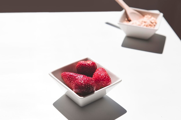 Vista minima di una ciotola di fragole rosse e avena su sfondo bianco piatto e spazio di copia