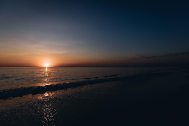 Vista mozzafiato del tramonto estivo sulla spiaggia. Meraviglioso paesaggio al tramonto sul mare scuro e profondo e il cielo arancione sopra di esso e le onde calme scorrono su di esso.
