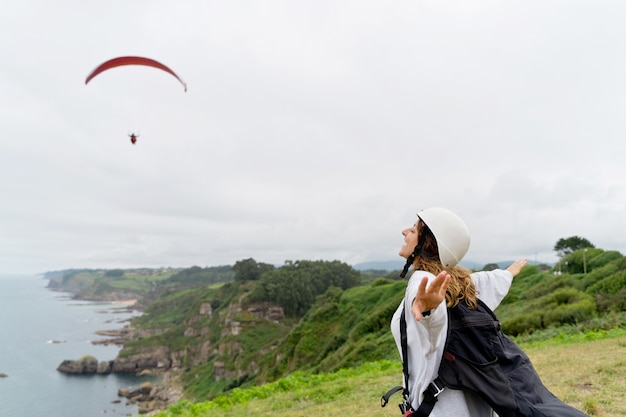 Vista orizzontale della donna caucasica con attrezzatura di parapendio su una scogliera. Vista panoramica della donna avventurosa che pratica sport rischiosi. Avventura e stile di vita sportivo.