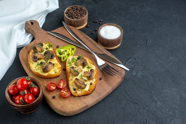 Vista orizzontale di deliziosi spuntini con verdure fresche di funghi e posate su tagliere di legno asciugamano bianco spezie su sfondo nero