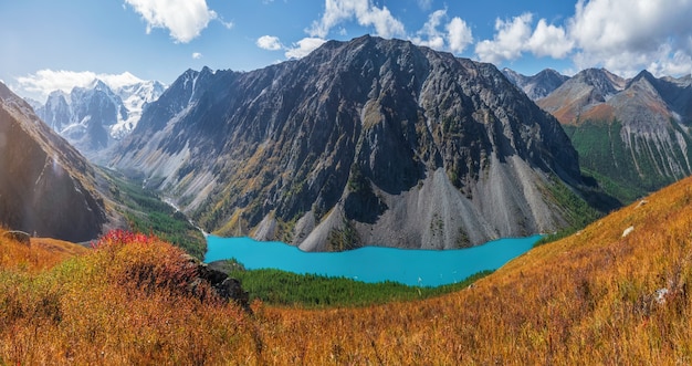 Vista panoramica autunnale al lago di montagna sullo sfondo delle montagne. Atmosferico paesaggio dorato con lago in alta valle di montagna. Lago Shavlinskoe inferiore nei Monti Altai.