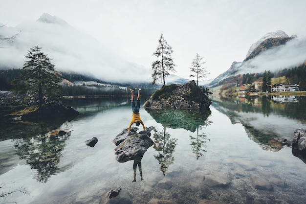 Vista panoramica del lago contro il cielo durante l'inverno con l'uomo che fa handstand in primo piano