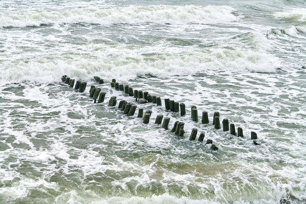 Vista panoramica del mare blu con onde spumeggianti e spumeggianti. Frangiflutti in legno lunghi vintage che si estende lontano verso il mare, paesaggio invernale del Mar Baltico