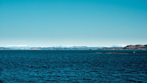 Vista panoramica del mare blu scuro con isola rocciosa e montagne sullo sfondo in Norvegia Giorno di primavera soleggiato