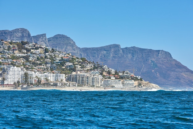 Vista panoramica del mare e del cielo blu sulla spiaggia di Camps Bay con le montagne dei Dodici Apostoli sullo sfondo Tranquillo oceano marino con spazio per la copia e infrastrutture per la costruzione di Città del Capo in Sud Africa