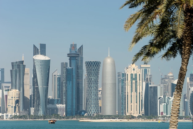 Vista panoramica del moderno skyline di Doha attraverso palme sfocate. Il Qatar il giorno pieno di sole.