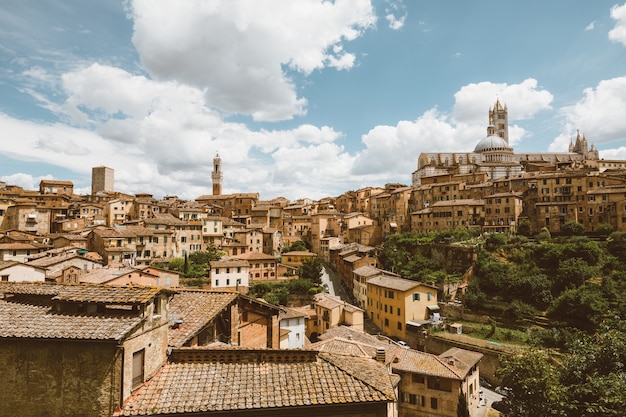 Vista panoramica della città di Siena con edifici storici e lontano Duomo di Siena (Duomo di Siena). Giornata di sole estivo e cielo blu drammatico