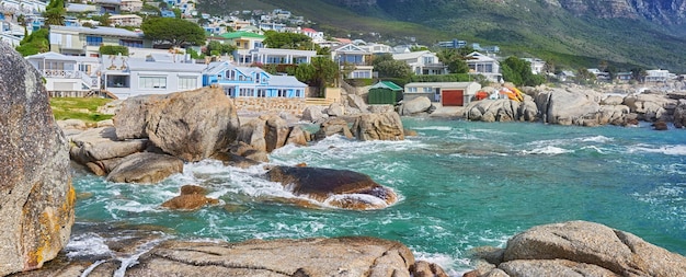 Vista panoramica delle rocce marine e degli edifici residenziali a Camps Bay Beach Città del Capo Sud Africa Le onde dell'oceano si infrangono sulle rocce e sui massi del litorale Destinazione di viaggio e turismo d'oltremare