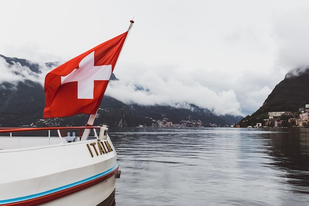 Vista panoramica sul lago di Lugano con Campione sullo sfondo e la bandiera della Svizzera davanti