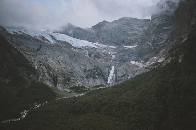 Vista panoramica sulla scena delle montagne e lontana cascata nel parco nazionale di Dombay, Caucaso, Russia. Paesaggio estivo, tempo soleggiato e giornata di sole