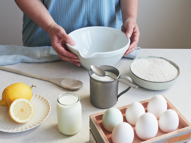 Vista parziale della persona con le mani sopra una ciotola pronta da cucinare con uova farina latte e limone sul piano di lavoro della cucina